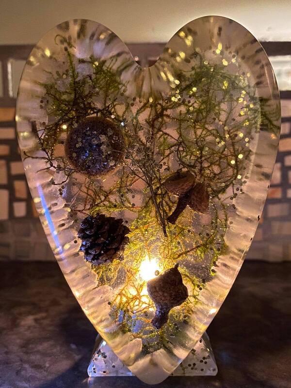 Close up of a Tall Heart memorial keepsake placed in front of a tealight candle, infused with irish moss, acorns, miniature cones, gold glitter and an Ash Orb suspended in resin, standing 4.5" tall approx 1.5" deep.